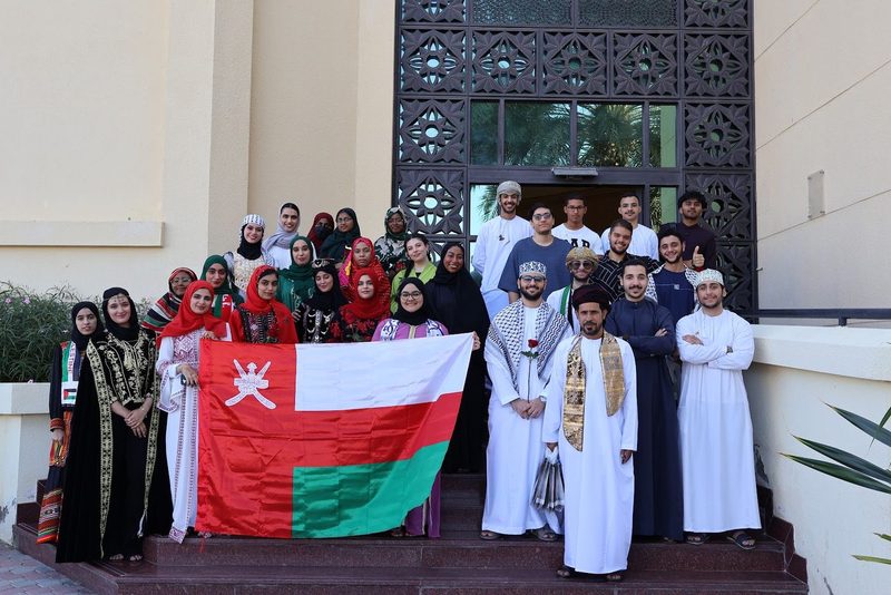 Members on the steps for National Day 2024, many in their countries' traditional dress, holding Oman's flag